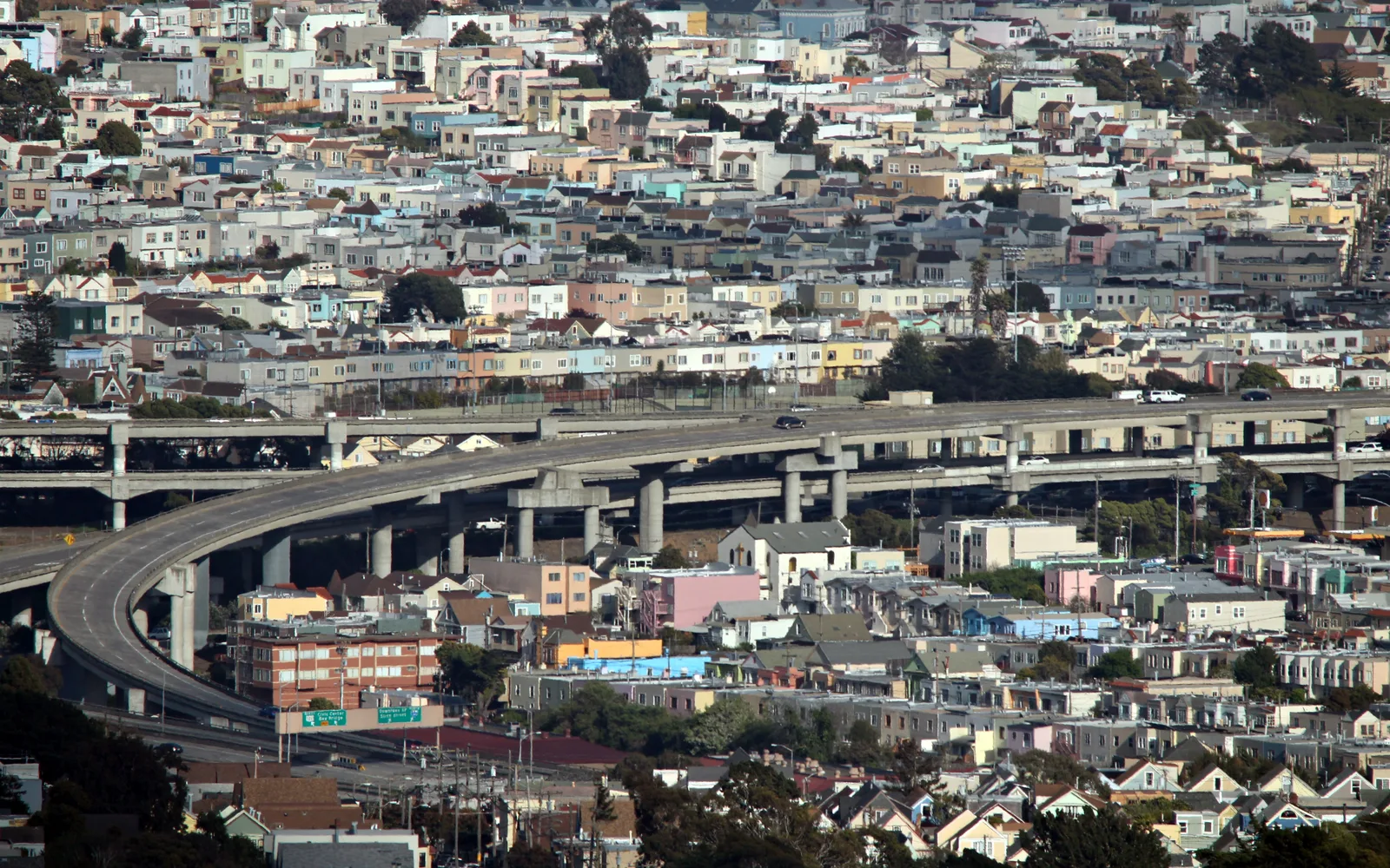 Elevated view of residential neighborhoods adjacent to a freeway, showing tree-lined streets and suburban homes